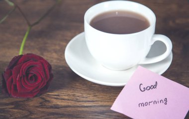 kırmızı gül ve bir fincan kahve ve kağıt üzerinde günaydın metni 