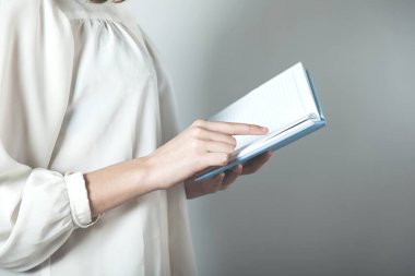 Gri arka planda elinde not defteri tutan kadın.