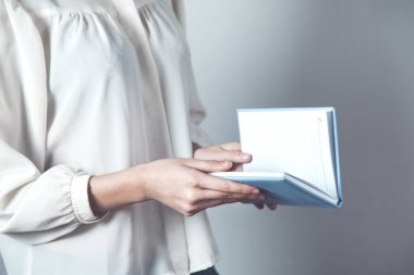 Gri arka planda elinde not defteri tutan kadın.