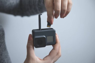 Gri duvar arka planında gopro tutan kadın.