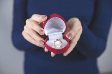 Gri arka planda yüzüğü olan kırmızı kutuyla el ele tutuşan kadın.