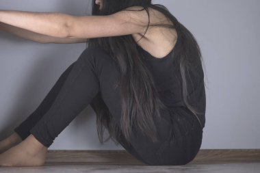 Gri arka planda yerde oturan üzgün kadın.