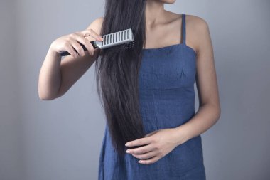 Genç kadın saçlarını gri arka planda tarıyor.