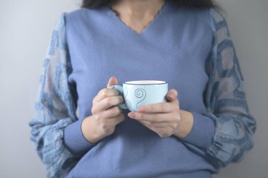 Gri arkaplanda bir fincan çay tutan kadın.