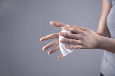 Kadın, gri arka planda peçeteyle elini temizledi.