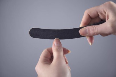 Kadın tırnaklarını gri arka planda törpülüyor