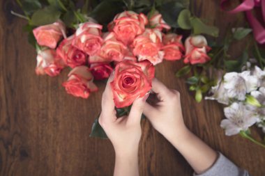 Kadın arka planda çiçekleri tutuyor.