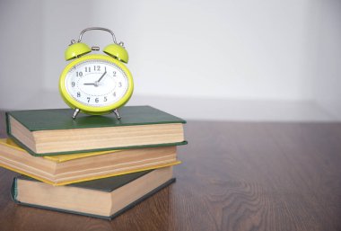 Kitaplar ve yeşil saat masanın üstünde.