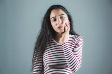 Gri arka planda dişi ağrıyan bir kadın.