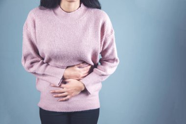 Gri arka planda karın ağrısı çeken bir kadın.