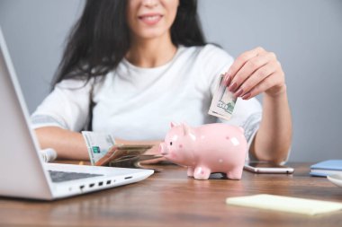 Kadın domuz kumbarasıyla birlikte çalışma masasında para veriyor.