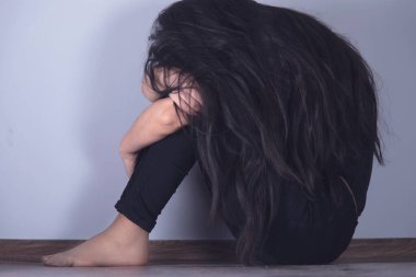 Gri arka planda yerde oturan üzgün kadın.