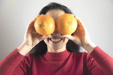 Mutlu kadın gri arka planda portakalı gözüne aldı