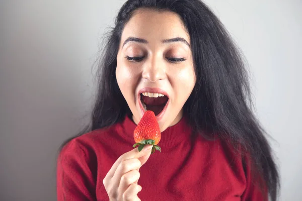 happy woman eat strawberries on grey background