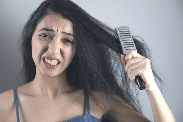 young woman combs the hair on grey background