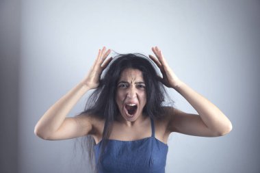 Öfkeli genç bir kadın gri duvarda bağırıyor.