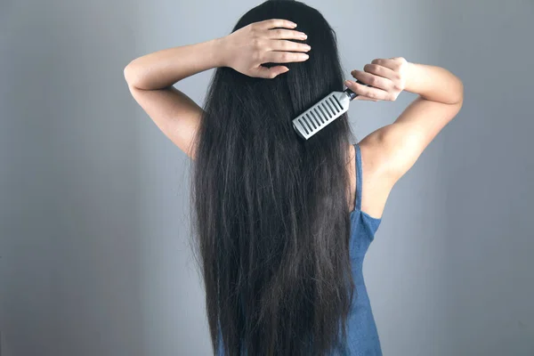 young woman combs the hair on grey background