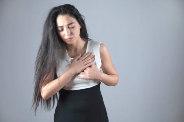 Gri arka planda, kalbi sızlayan genç bir kadın.