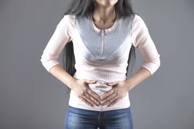 Gri arka planda karın ağrısı çeken kadın.