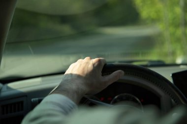 Adam asfalt yolda yeşil ağaçlı bir araba kullanıyor.