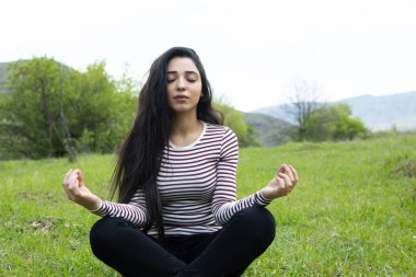 Yeşil çimlerde oturan meditasyon yapan kadın.