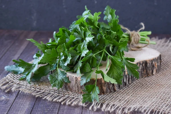 Fresh bundle of greenery on a wooden background. Parsley for salads. Appetizing green greens for dishes.