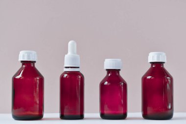 Kozmetik ürünleri için cam şişeler, doğal ilaçlar, gerekli yağlar veya pembe arka planda izole edilmiş diğer sıvılar. Kozmetik ve ilaçlar için cam şişeler. Doğal katkı maddeleri için bir kavanoz.