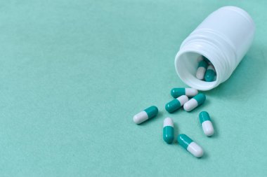 Beslenme takviyeleri. Peluli plastik kutunun yanında. Açık bir şişenin önünde yeşil arka planda kapağı olmayan birkaç uzun kapsül. Kapak ve antivirüs koruması.