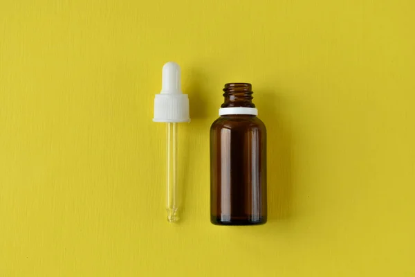 Glass vials for cosmetics, natural medicine, essential oils or other liquids isolated on a yellow background, top view cosmetic bottle glass dropper with white rubber