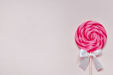 Pembe parlak bir lolipop ve beyaz bir fiyonk..