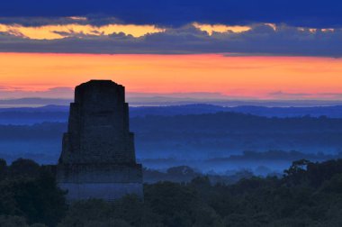 View of a sunrise above the Peten jungle with the pyramids of Tikal towering above the tree canopy in Guatemala. clipart