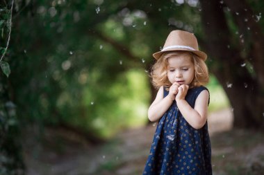 girl in a straw hat looks at poplar fluff