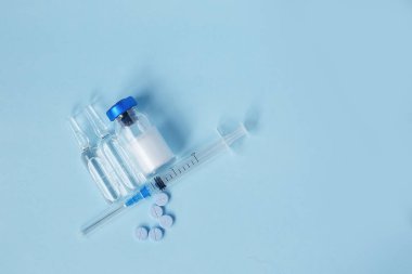 Mavi arka planda cam şişelerde şırınga ve ilaç.