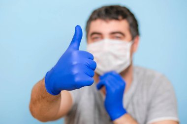 Tıbbi maskeli ve mavi eldivenli bir adam. El hareketi dersi. Mavi arkaplan.