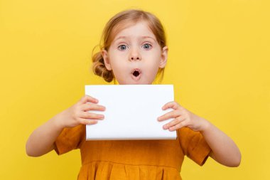 Sarı arka planda açık renk saçlı küçük bir kız. İzole edilmiş. Sarı elbiseli bir çocuk bir kitabın üzerine notlar alır. Model.