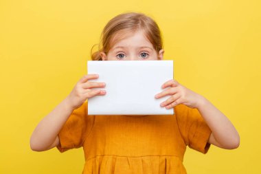 Sarı arka planda açık renk saçlı küçük bir kız. İzole edilmiş. Sarı elbiseli bir çocuk bir kitabın üzerine notlar alır. Model.