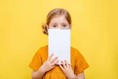 Sarı arka planda açık renk saçlı küçük bir kız. İzole edilmiş. Sarı elbiseli bir çocuk bir kitabın üzerine notlar alır. Model.