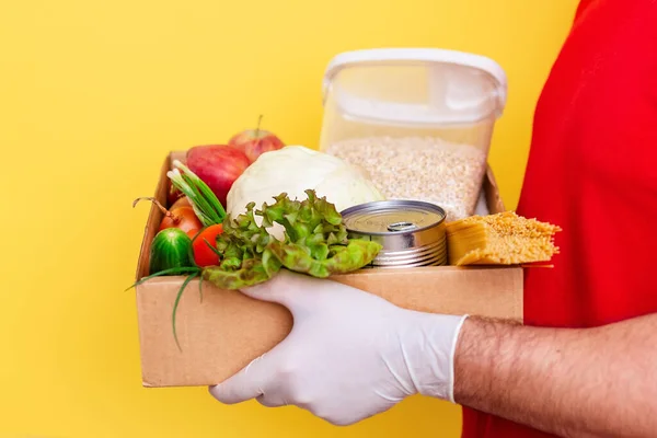 Волонтер приносить коробку з їжею. Свіжі овочі та продукти в картонній коробці на жовтому тлі, пожертвування . — стокове фото