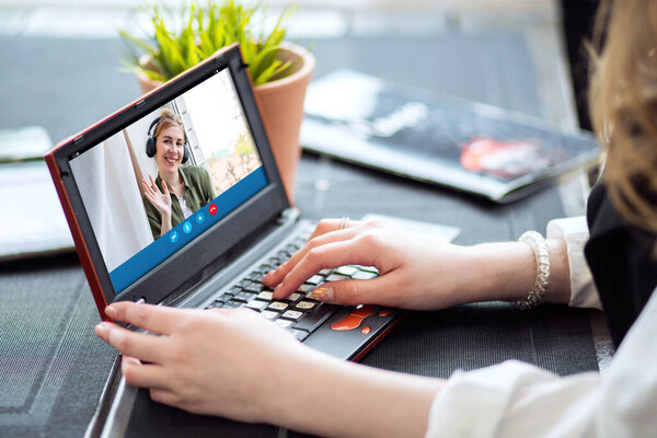 A happy blonde woman using a laptop computer to video call friends and parents, a girl sitting at home on the window