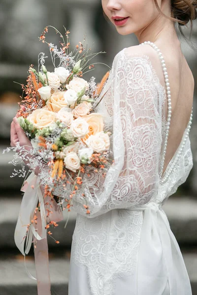 Elegantní krásná kytice z bílých a béžových růží v rukou nevěsty. Svatební kytice v jejích rukou. — Stock fotografie
