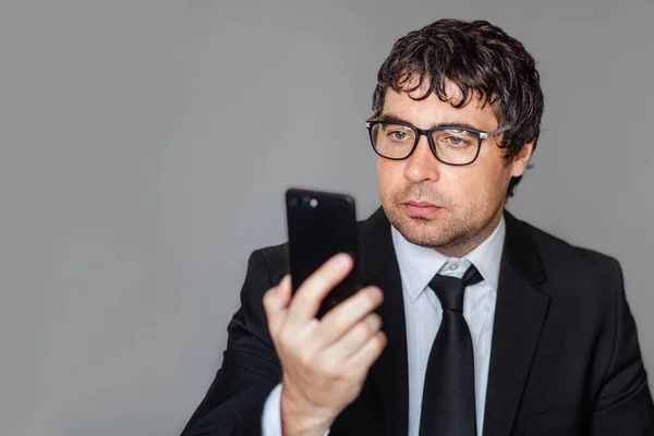 A male businessman in a black suit and glasses is talking on the phone. Grey isolated background.