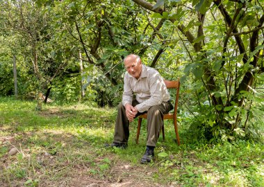 Sandalyede oturan gülümseyen kıdemli adam.