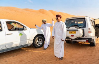 Wahiba Sands, Umman - 12 Şubat 2020: Geleneksel giyinmiş Mutlu Umman erkekleri, Umman Sultanı Wahiba Kumları Çölü 'nde beyaz 4x4 off-road arabalarıyla eğleniyor..