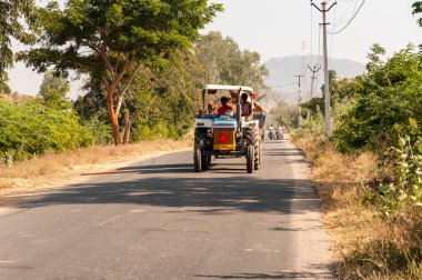 Puttaparthi, Andhra Pradesh, Hindistan - 12 Ocak 2013: Hindistan 'ın Puttaparthi köyüne giden yolda traktördeki Hintli işçiler odunları taşıyor