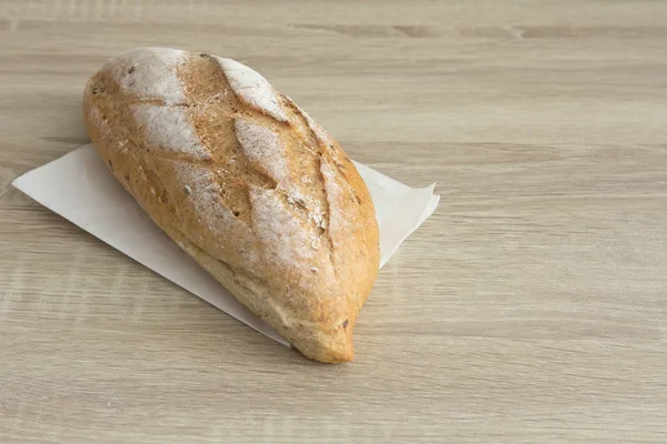 Brown crusty french loaf bread on whit paper on a wood table.
