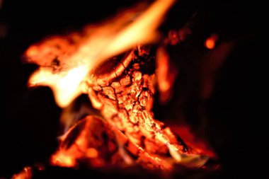 An intimate close-up image capturing the flickering flames and glowing embers of burning wood, showcasing the mesmerizing interplay of light and heat in a cozy fire setting.