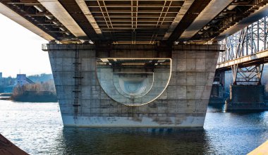 This image showcases an architectural view underneath a bridge, highlighting its concrete structure and geometric patterns, portraying modern engineering and design concepts.