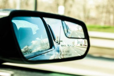 This image captures a car's side mirror reflecting the sky and road, highlighting the dynamic interaction between motion and stillness in everyday driving experiences.