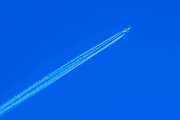 Modern jet plane with white condensation track flies on a blue sky background — Stock Photo, Image