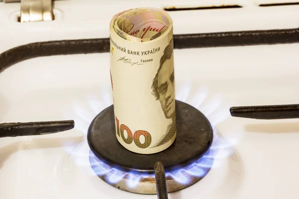 Pila di cento note grivna su una stufa a gas nel centro del comfort del gas, ustioni da gas . — Foto Stock